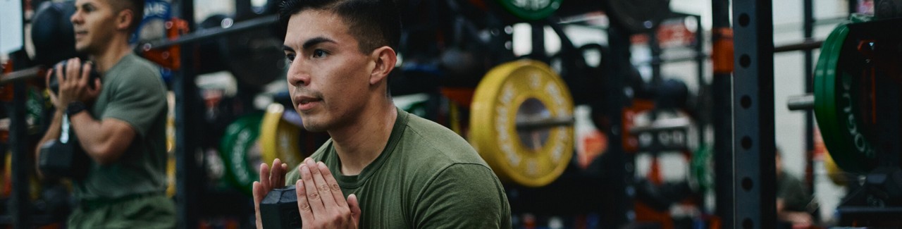 Two U.S. Marines exercise with weights in a gym. 
