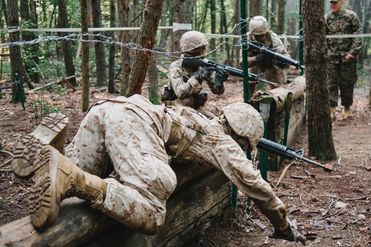 Marine Officer Candidates in woodland camouflage complete an obstacle course. 