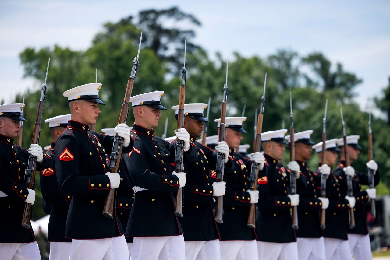 U.S. Marines in dress blues with rifles stand in formation.  