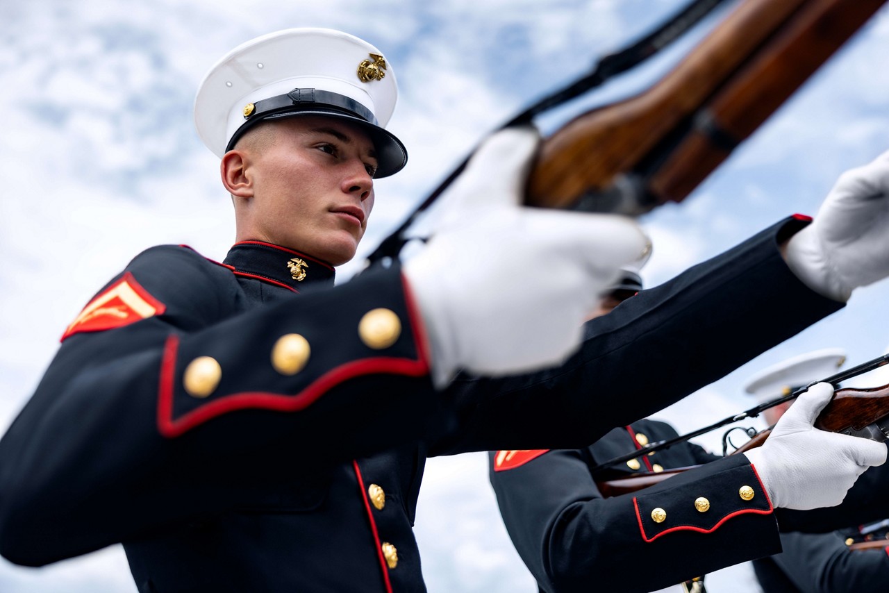 A U.S. Marine in dress blues holds a rifle.  