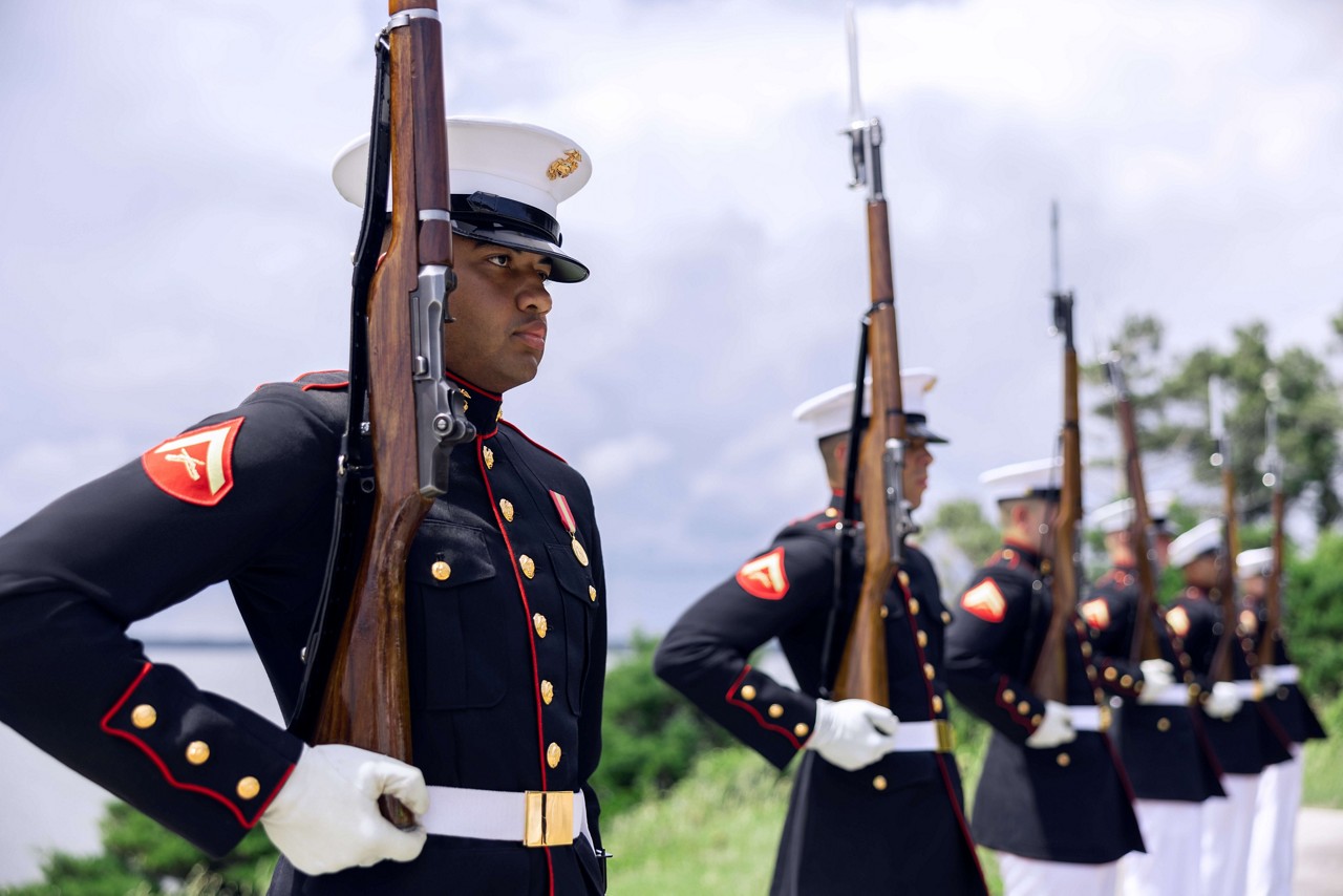 A platoon of U.S. Marines in dress blues hold rifles. 