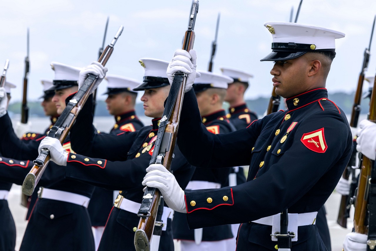 A platoon of U.S. Marines in dress blues spin rifles during a ceremony.  