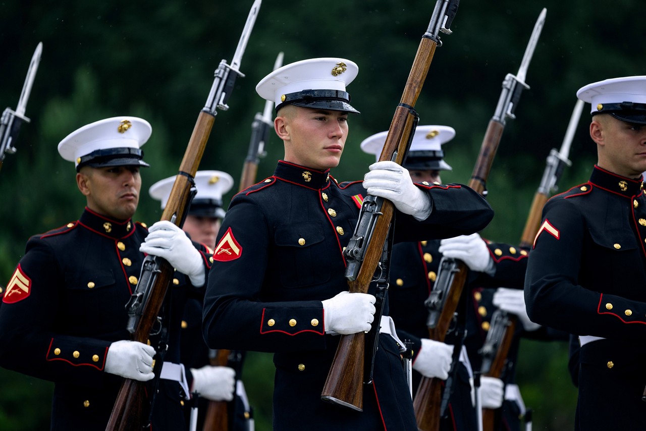 A platoon of U.S. Marines in dress blues spin rifles during a ceremony.  