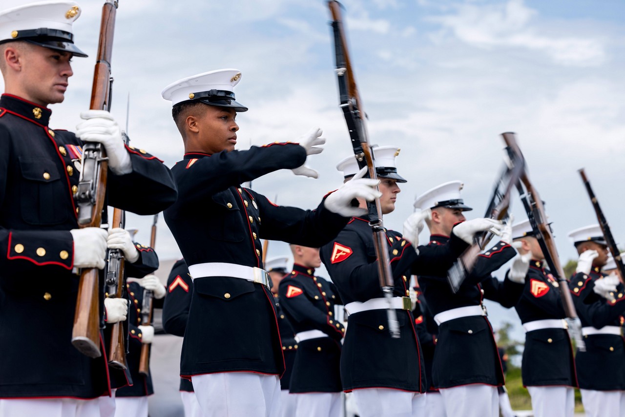 A platoon of U.S. Marines in dress blues spin rifles during a ceremony.  