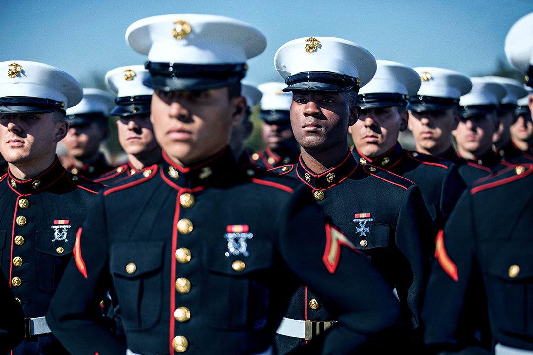 U.S. Marines in dress blue uniforms standing in formation during ceremonial event.