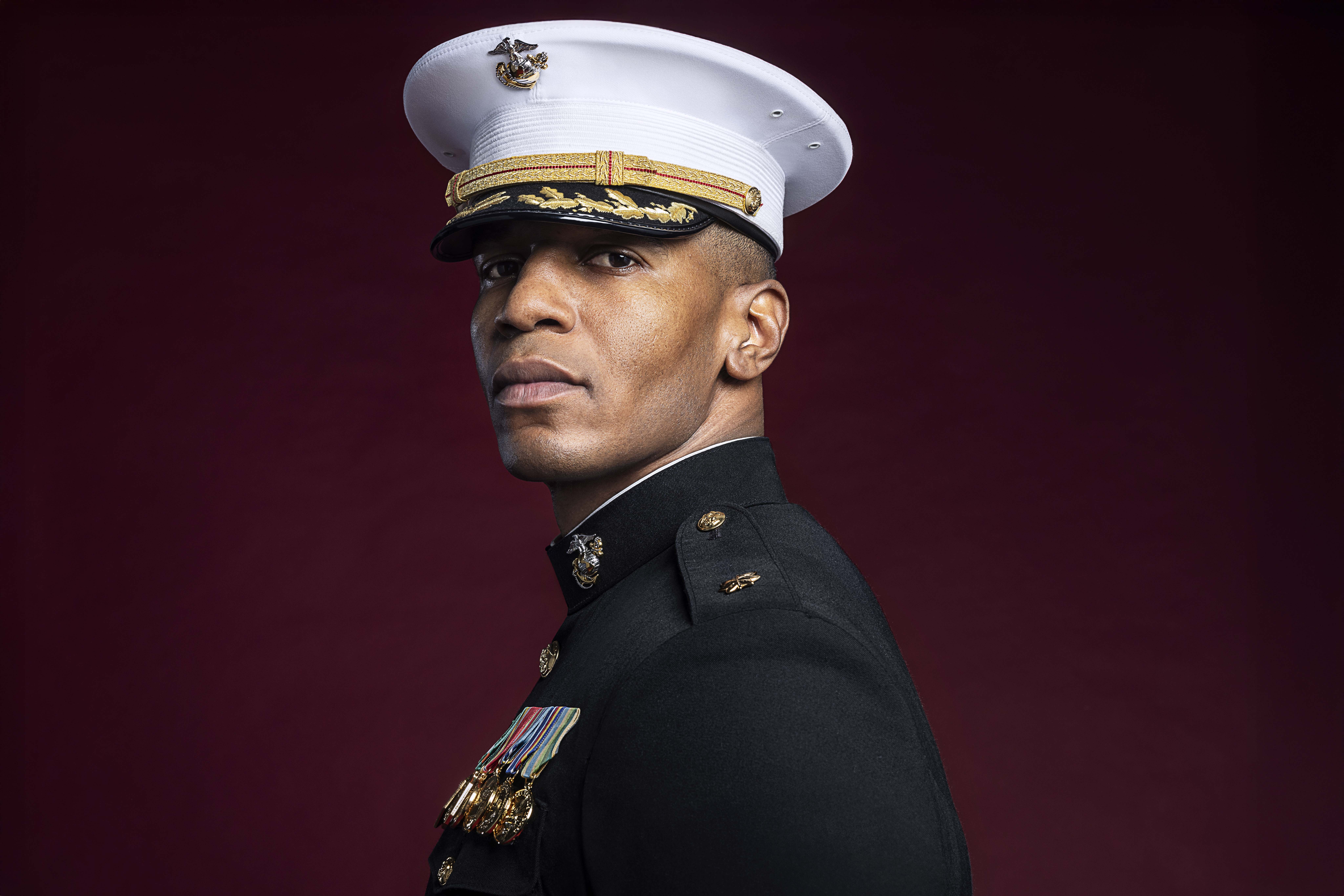 Marine officer in dress blue uniform with white cover and gold insignia in formal portrait.