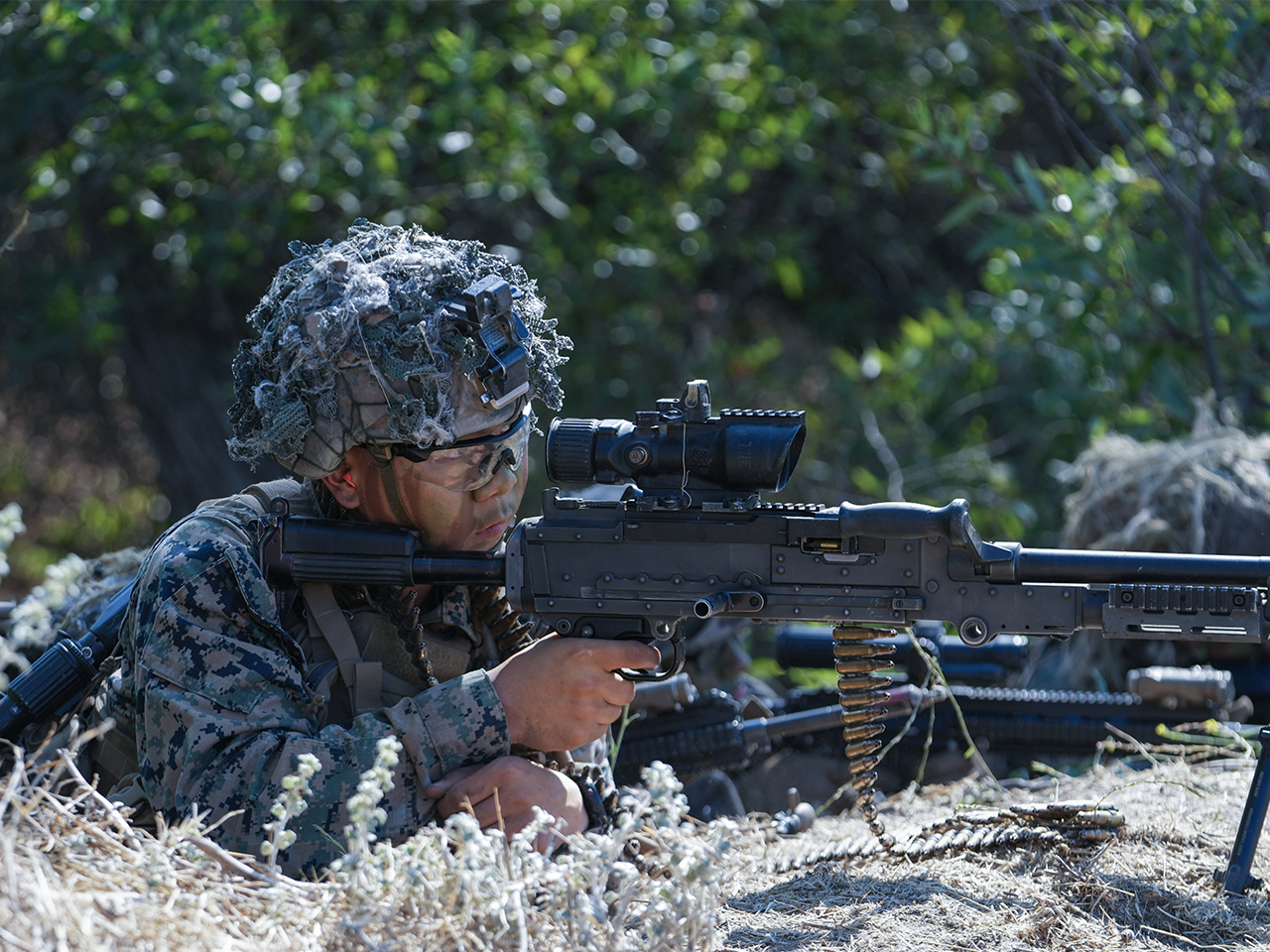Marine in camouflage with ghillie helmet operating machine gun during combat training at Camp Pendleton.