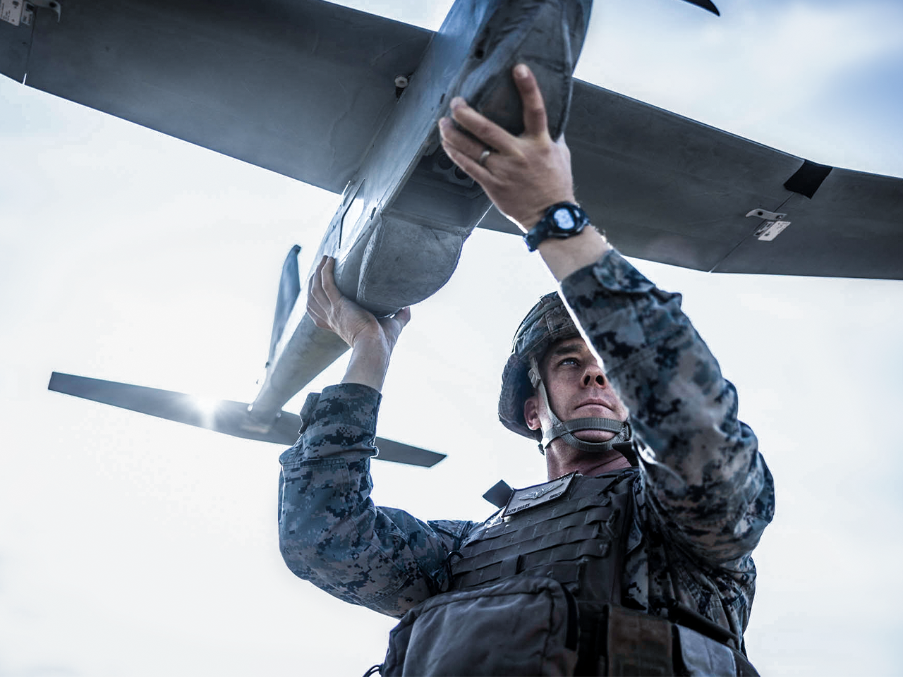Marine in camouflage and tactical vest inspecting military aircraft wing during maintenance operations.