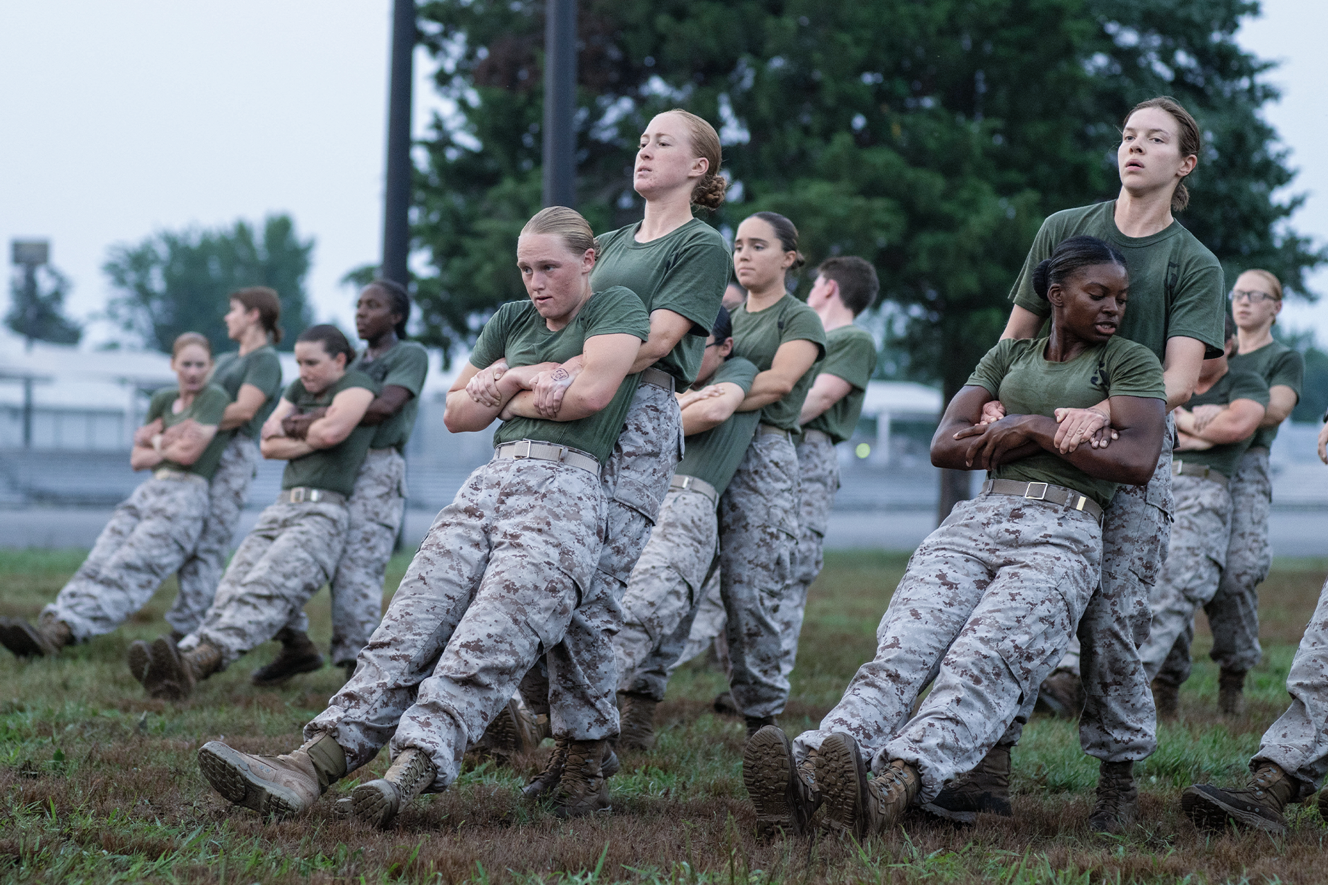 Female Marine recruits practicing martial arts techniques in camouflage pants and green shirts outdoors. 