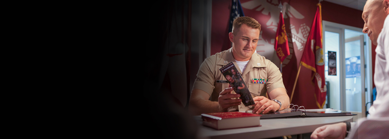 Marine officer in dress uniform with service ribbons consulting with person at desk in recruiting office.