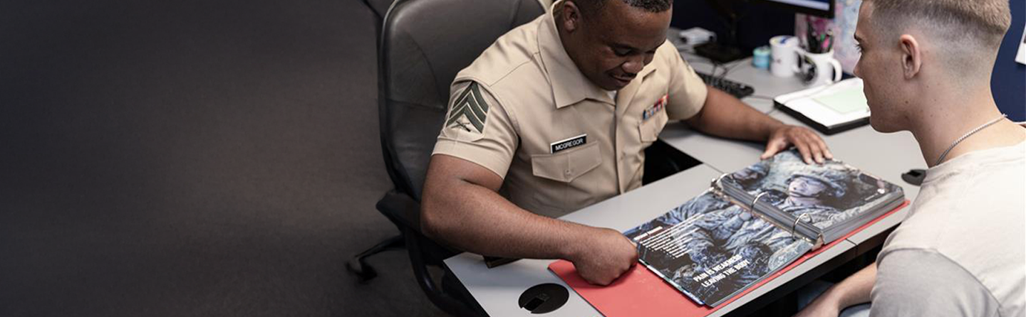 Marine recruiter with chevron insignia discussing materials with future Marine in Delayed Entry Program.