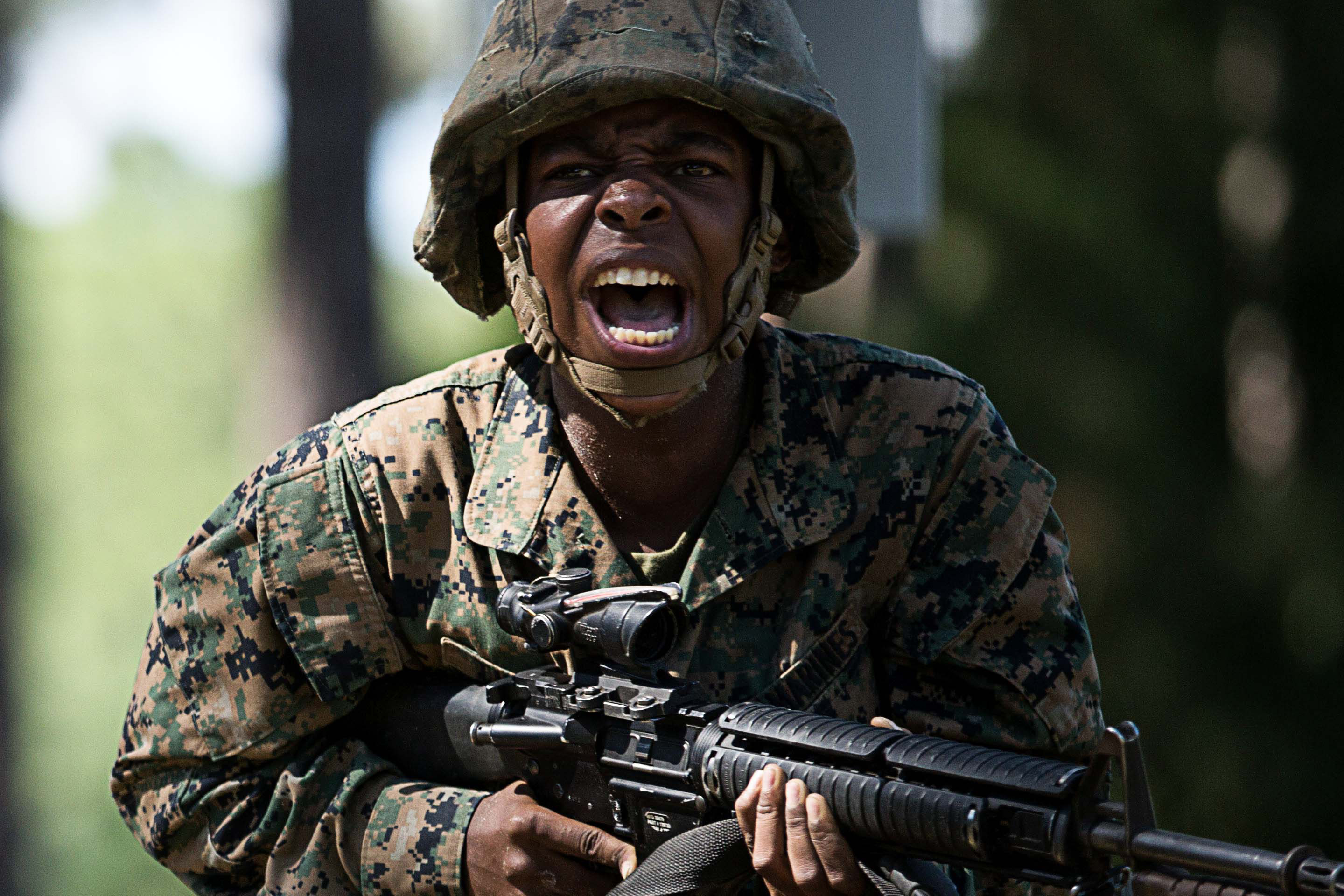  Marine Recruit carries a rifle during combat training exercise through dirt and obstacles. He is yelling fiercely as they run.