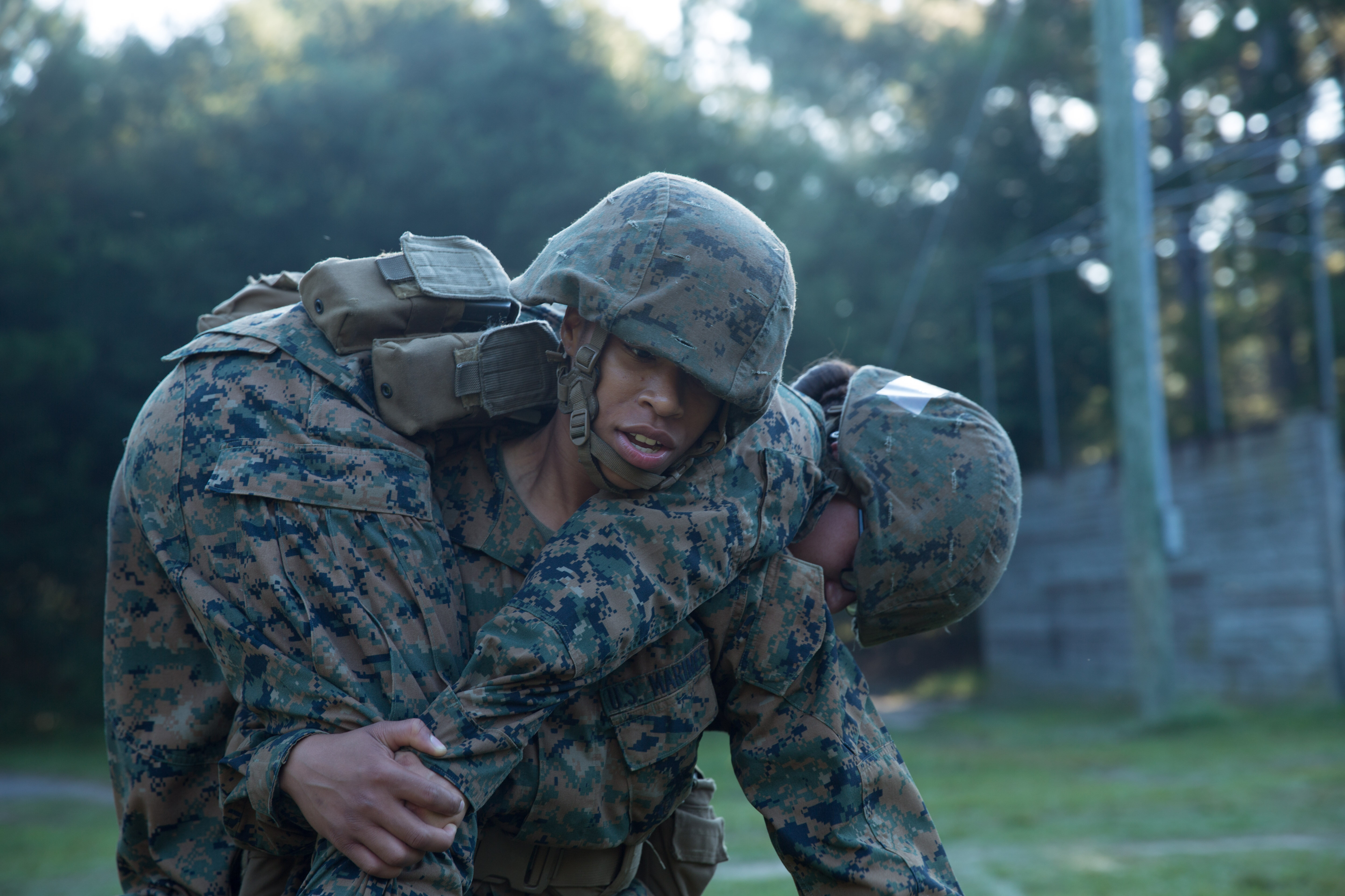 Marine officer candidates in camouflage utilities and helmets work together to move a rope across a barrel-and-plank water obstacle at the Leadership Reaction Course.