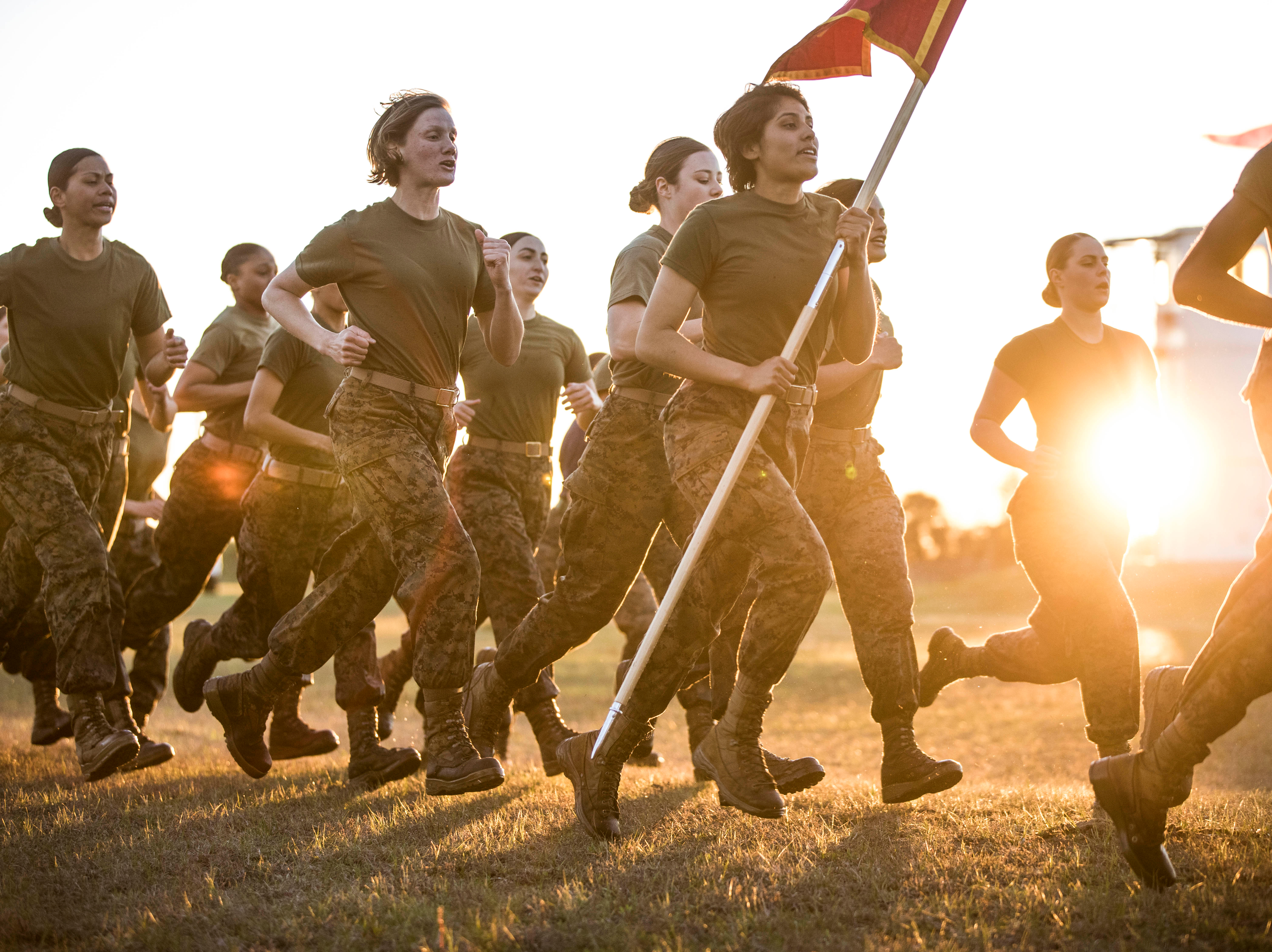  A group of female Marines run together in the early morning. One of the Marines carries a guidon. 
