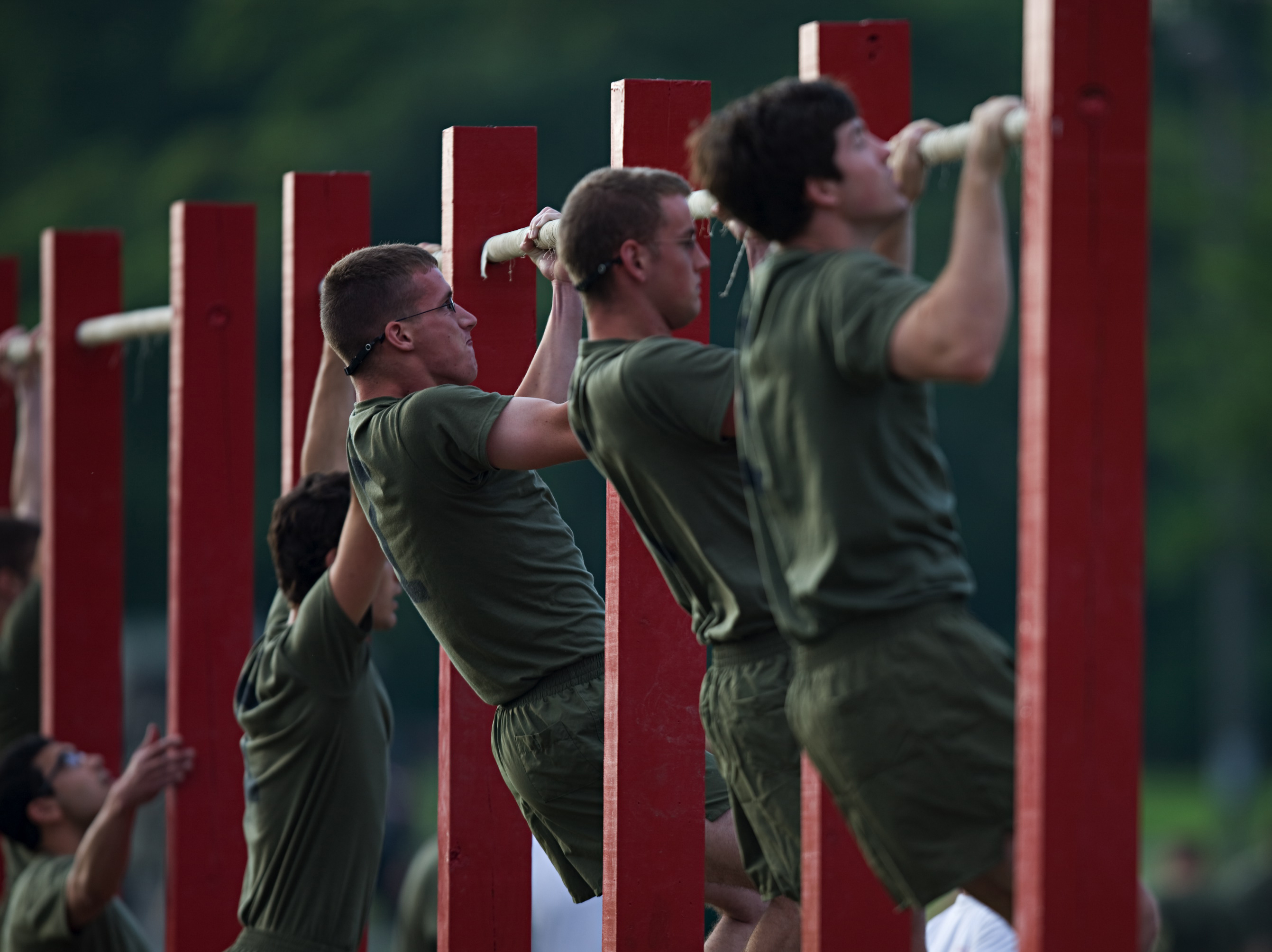  Male Marines complete pull-ups on pull-up bars during the physical fitness test. Other Marines watch them complete the assessment. 