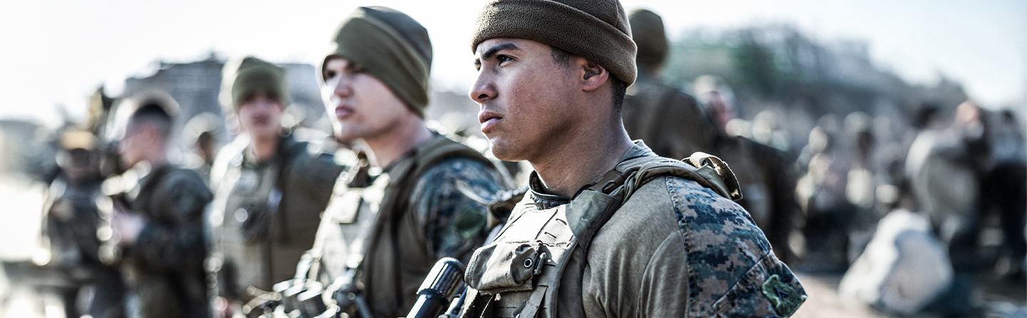 Marine in uniform looking ahead with fellow Marines in background, representing unity and shared purpose.