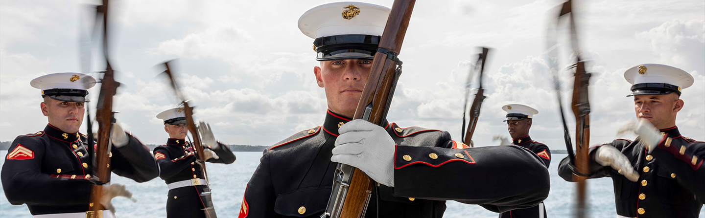 Marines in dress blue uniforms with white covers performing ceremonial duties during formal military ceremony.