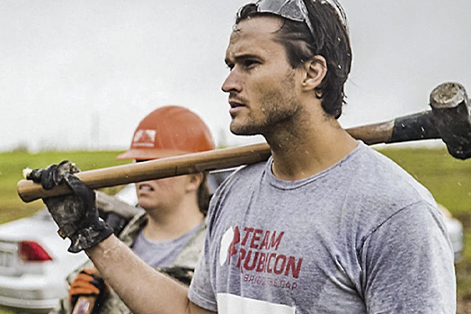 Jake Wood, the founder of Team Rubicon, walks with other disaster relief volunteers. He carries a mallet. 
