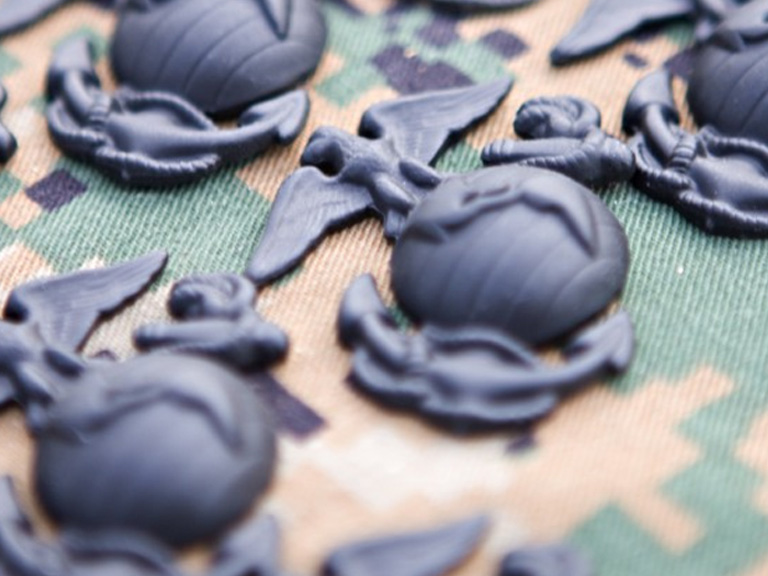 Dark gray Marine Corps emblems (eagle, globe, and anchor) scattered on a green and brown camouflage fabric.