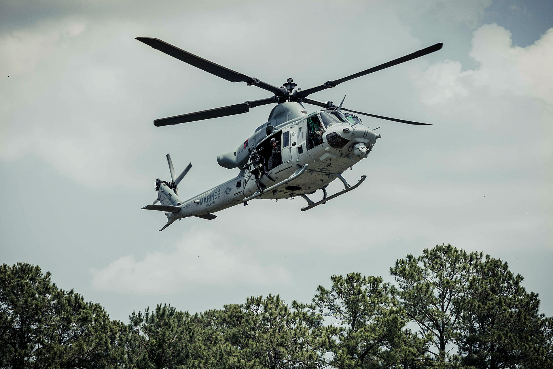 UH-1Y Venom utility helicopter with crew in open doors flies over tree line during training at Camp Lejeune.