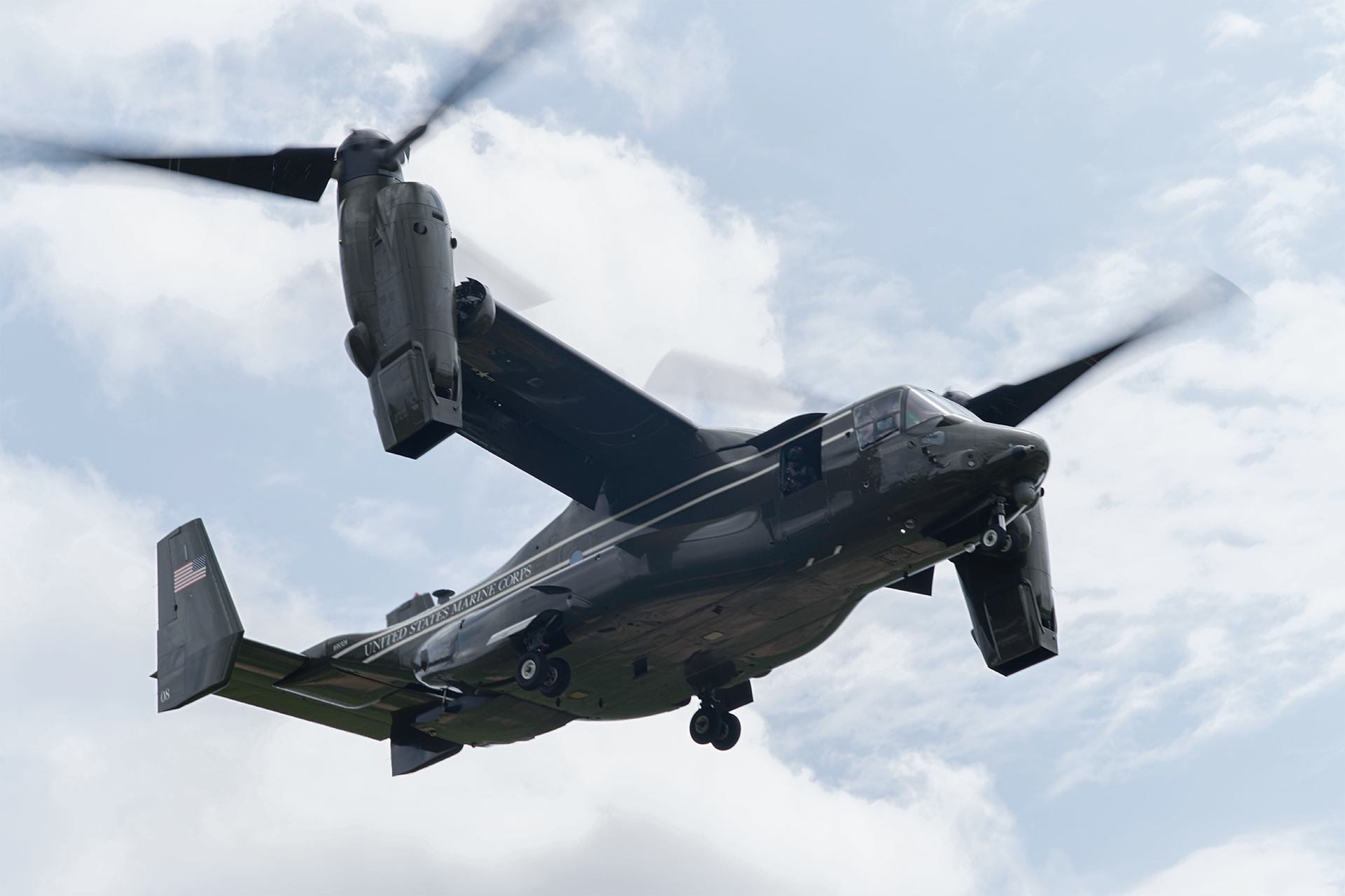 MV-22 Osprey tiltrotor aircraft flies with rotors in vertical position during training operations against cloudy sky.