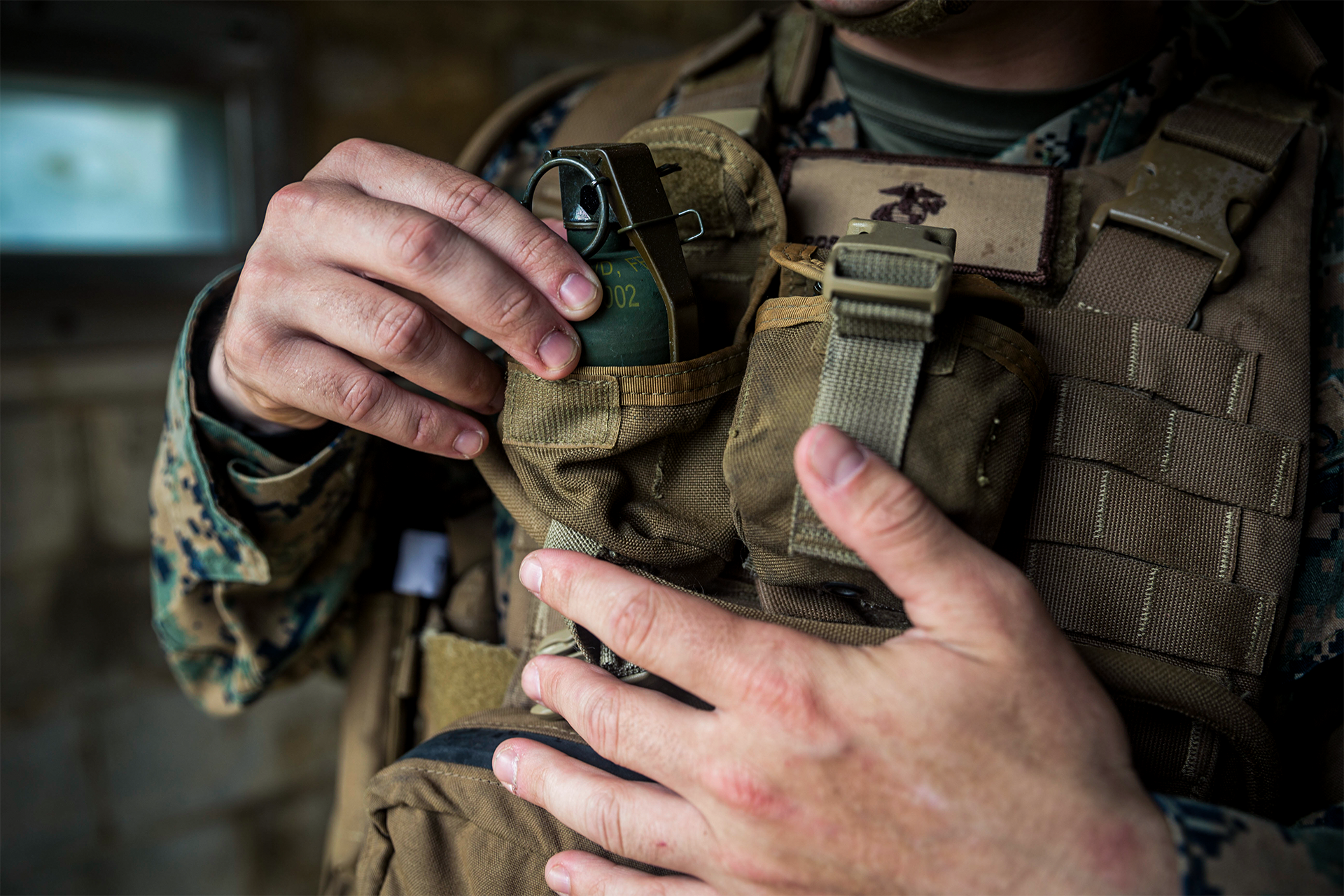 Marine removes training grenade from tactical pouch attached to plate carrier vest during equipment demonstration.
