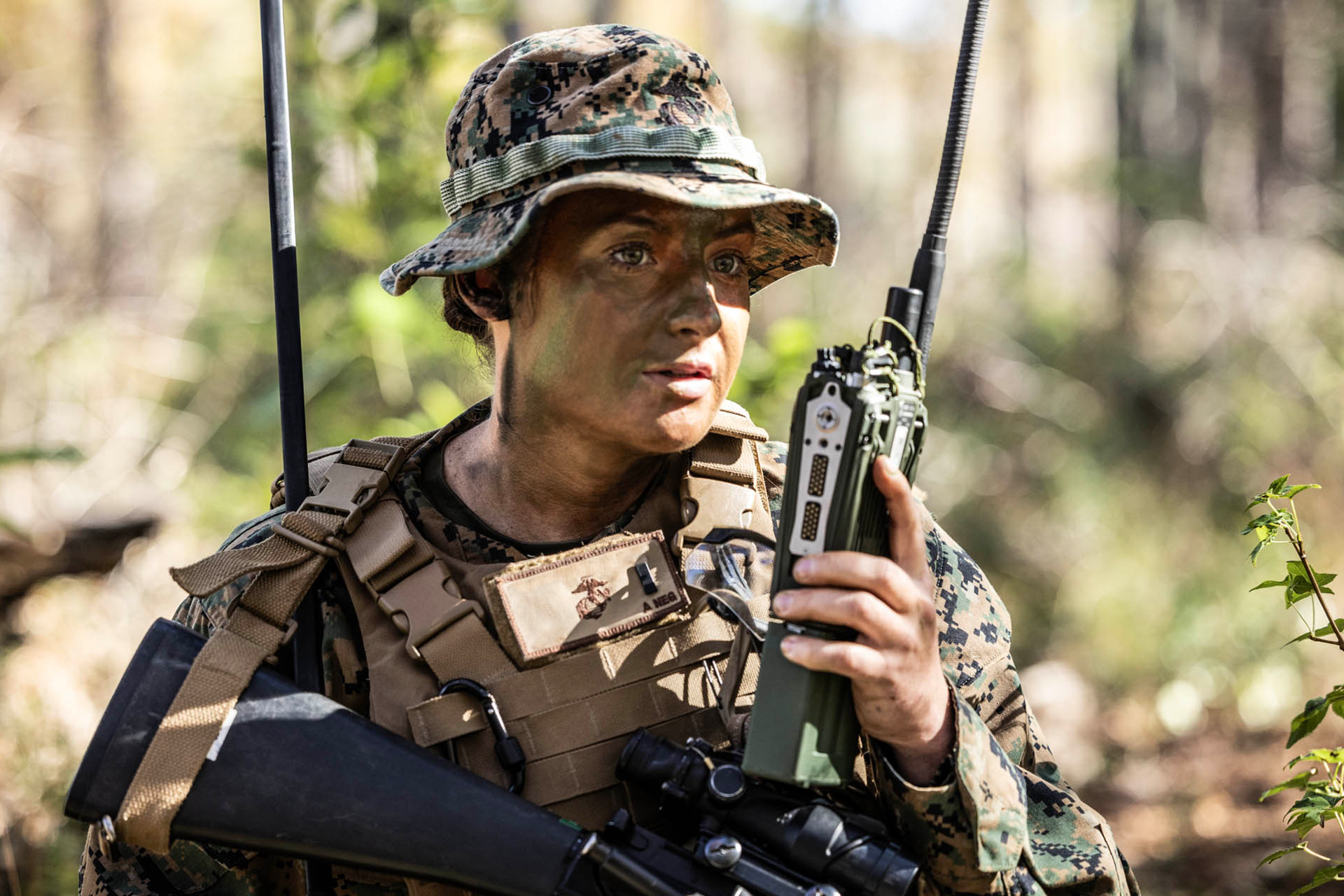 Marine uses tactical radio for communications during field training exercise wearing boonie hat and plate carrier.