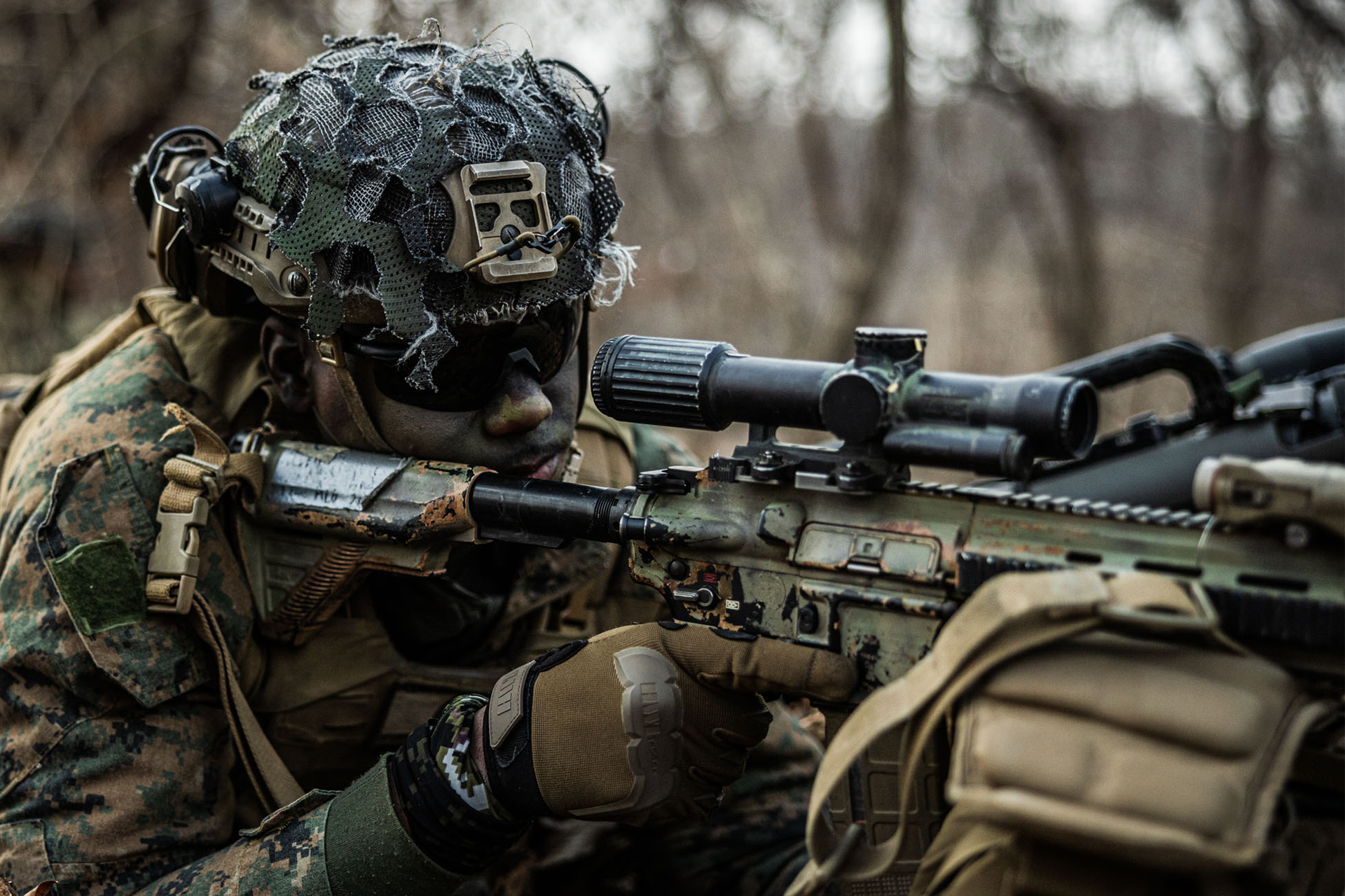 Marine aims rifle with magnified scope and camouflage covering helmet during training in South Korea.