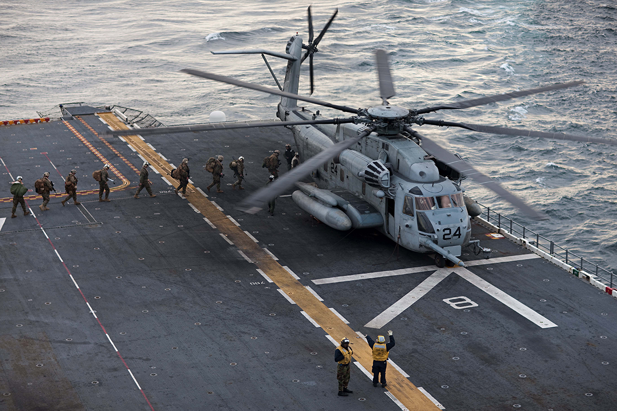 Marines board CH-53 helicopter on amphibious assault ship flight deck during Marine Expeditionary Unit operations at sea.