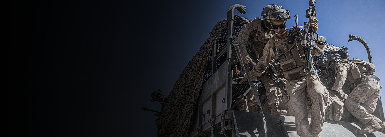 Marines in full combat gear climb down from armored vehicle during training exercise under clear blue sky.