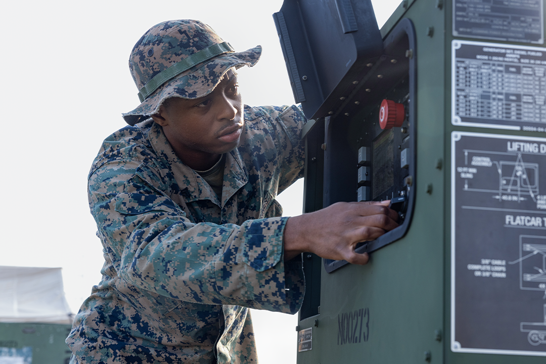 A utilities technician Marine opens up and inspects the control panel of a generator. 