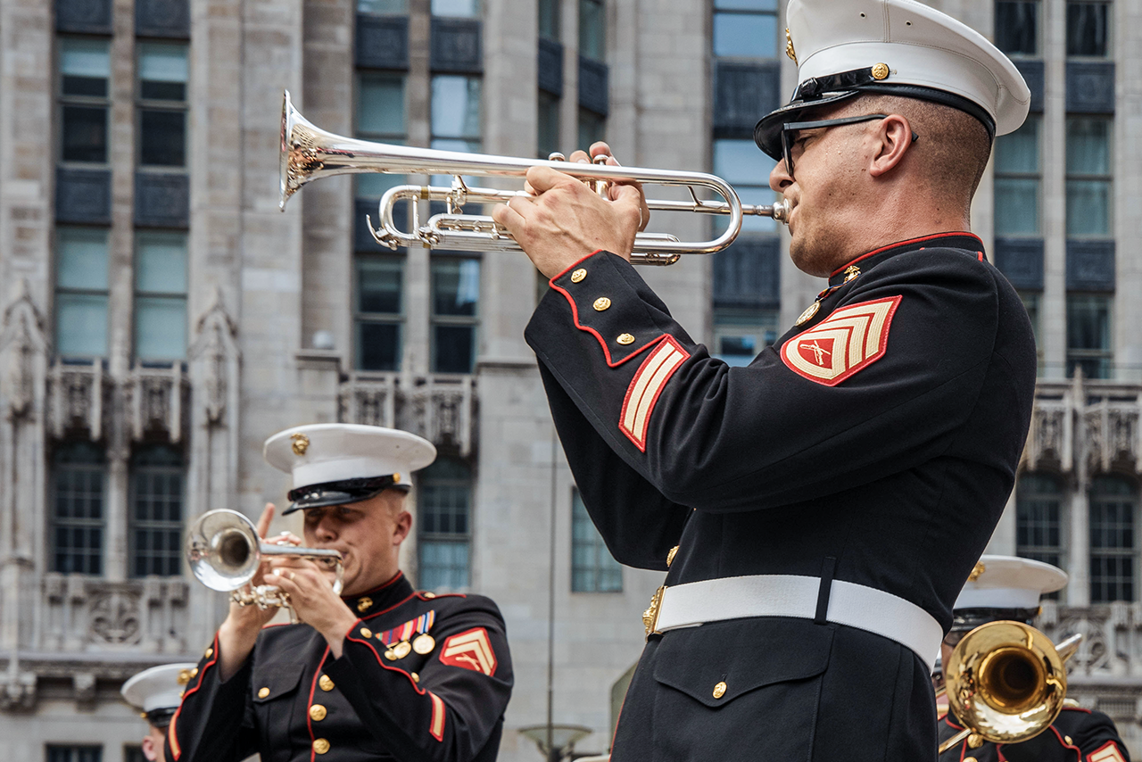 Marines in dress blues playing trumpet and brass instruments during ceremonial performance for the Marine Corps Band.