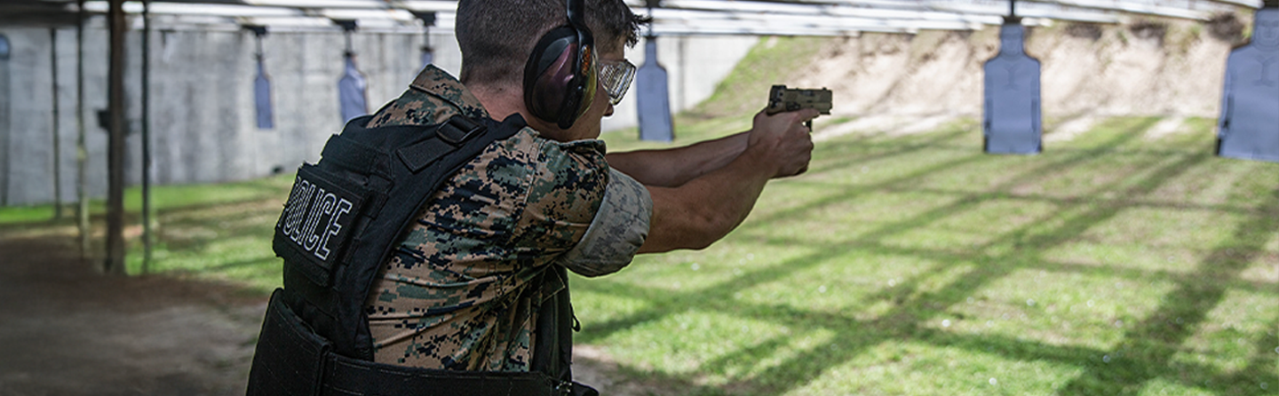 A law enforcement Marine practices his marksmanship at a firing range as he fires a pistol at a target.