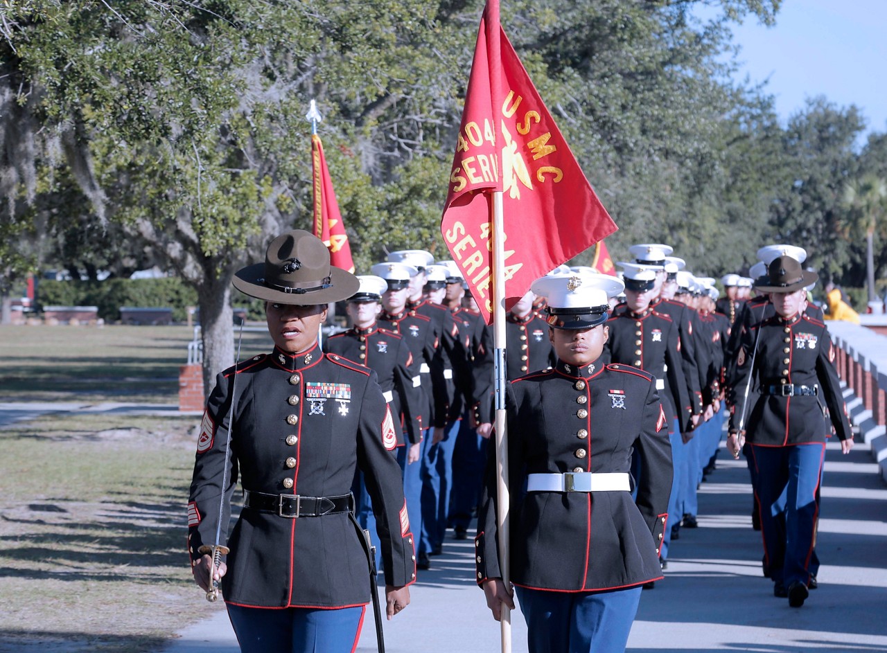 Marines walking in formation while holding USMC flag.