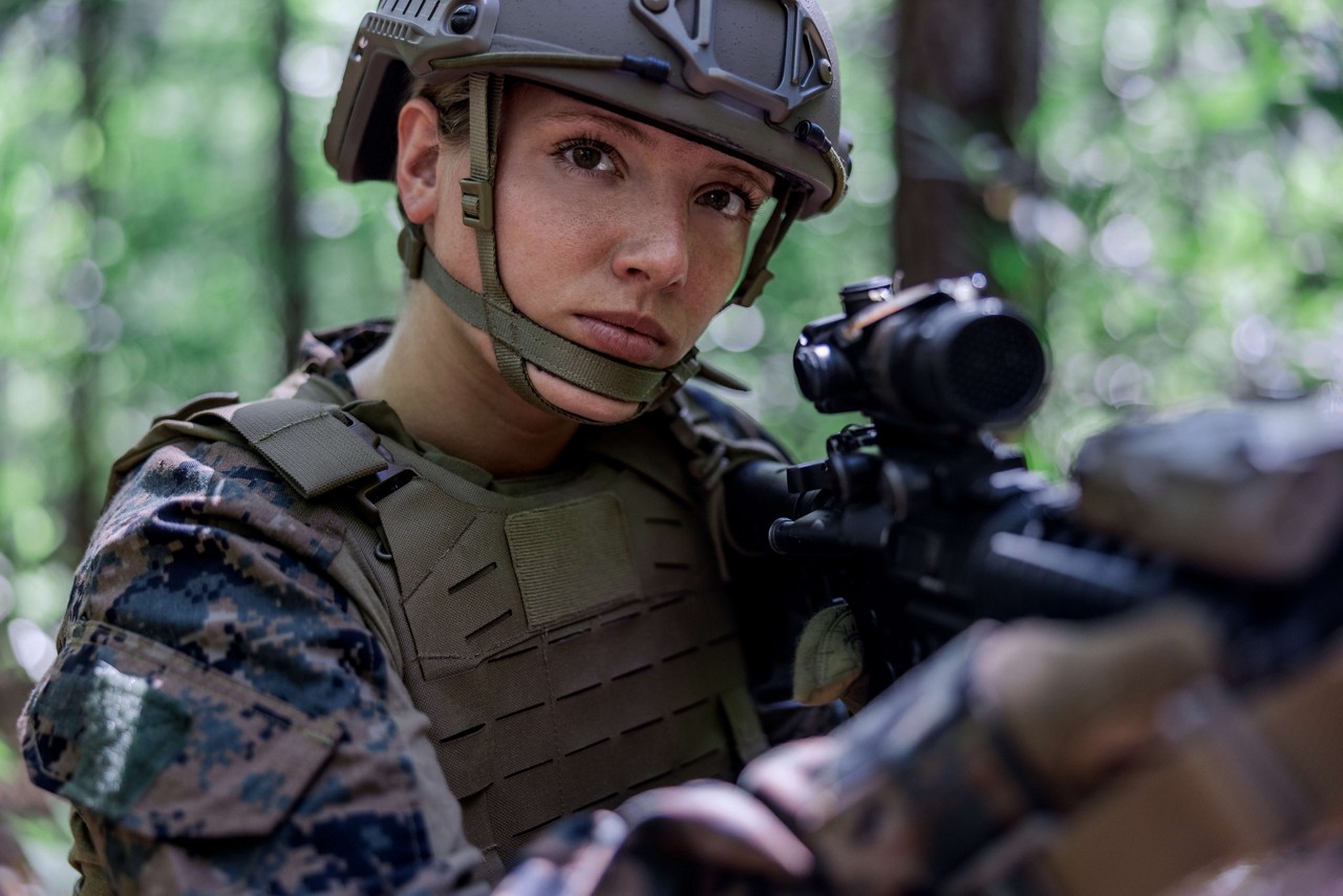 A U.S. Marine aims a rifle in a woodland environment. 